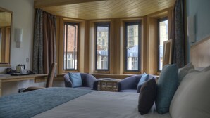 A hotel room with a large bed, a desk, and a view of buildings through the windows. - Canterbury Cathedral Lodge (Canterbury)