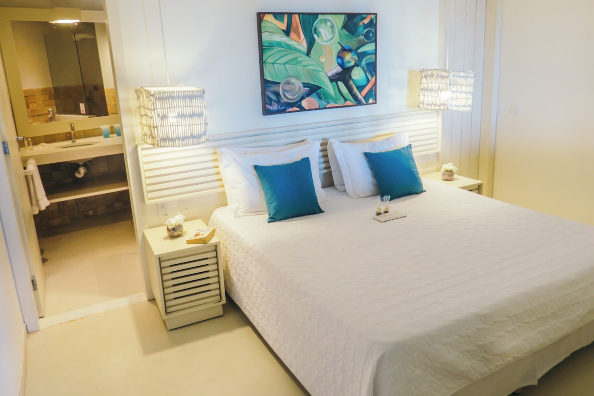 Een hotelkamer met een groot bed, twee nachtkastjes, een spiegel en een schilderij aan de muur.