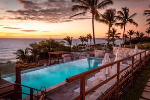 A pool area with a wooden deck, lounge chairs, and umbrellas, overlooking the ocean at sunset. - Pipa Privilege Suítes (Tibau do Sul)