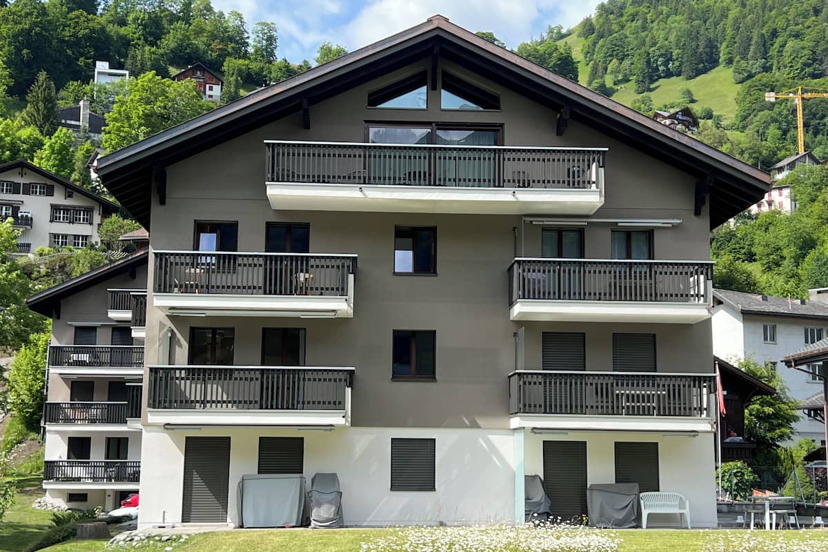 Un immeuble à plusieurs étages doté de balcons, d’un espace extérieur aménagé et couvert, et offrant une vue sur une colline verdoyante.