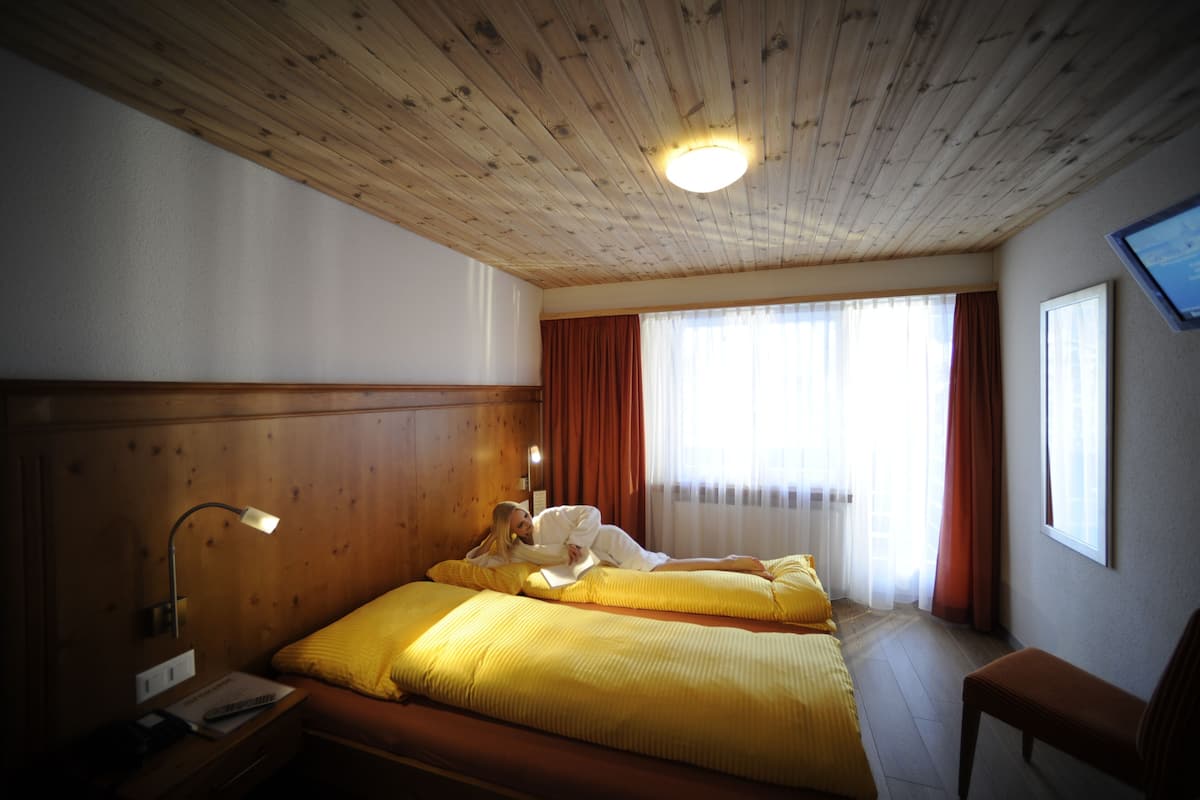 Une chambre d’hôtel avec des lambris en bois, un lit avec une literie jaune, une table de chevet avec une lampe et une fenêtre avec des rideaux.