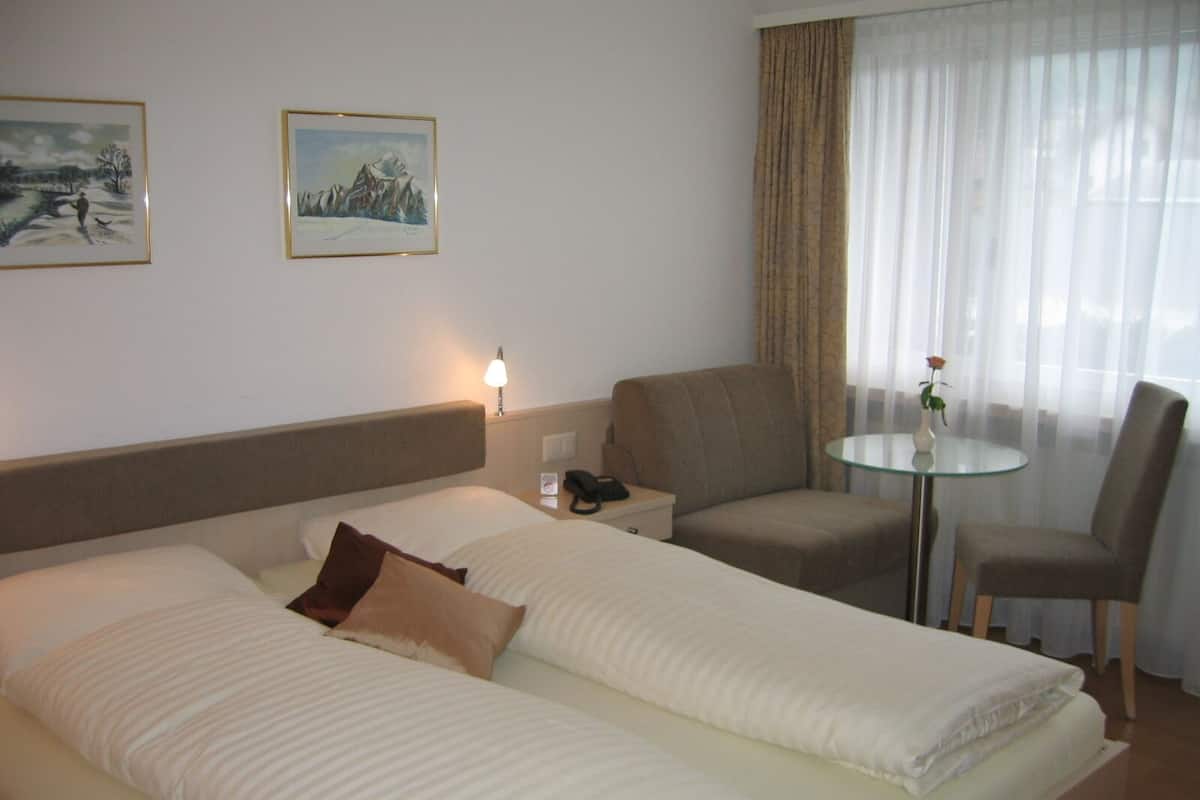 Une chambre d’hôtel avec deux lits, un coin salon avec une table et des chaises, et deux tableaux encadrés au mur.