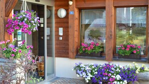 A wooden building with a number 54 sign, large windows with flower boxes, and a hanging flower basket.