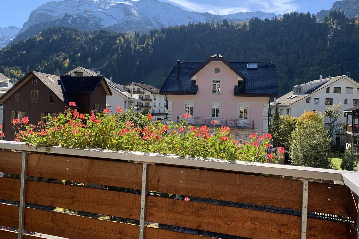 Un village de montagne aux maisons traditionnelles, doté d’une clôture en bois et offrant une vue sur des montagnes enneigées.