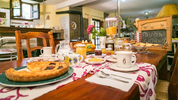 Una mesa de desayuno lista, con tarta, tazas de café y un frutero.
