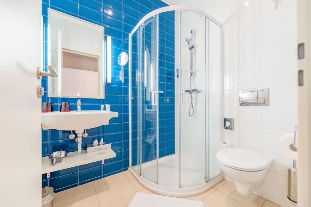 Un baño con cabina de ducha de vidrio, inodoro blanco y lavamanos con espejo.
