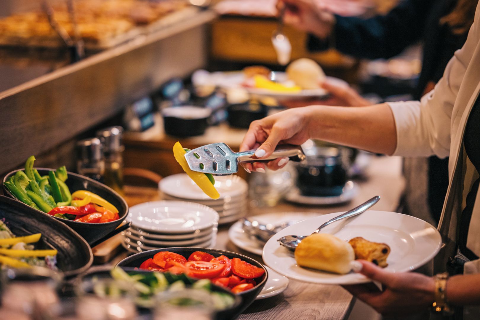 A buffet setup with various food items and a person serving themselves.
