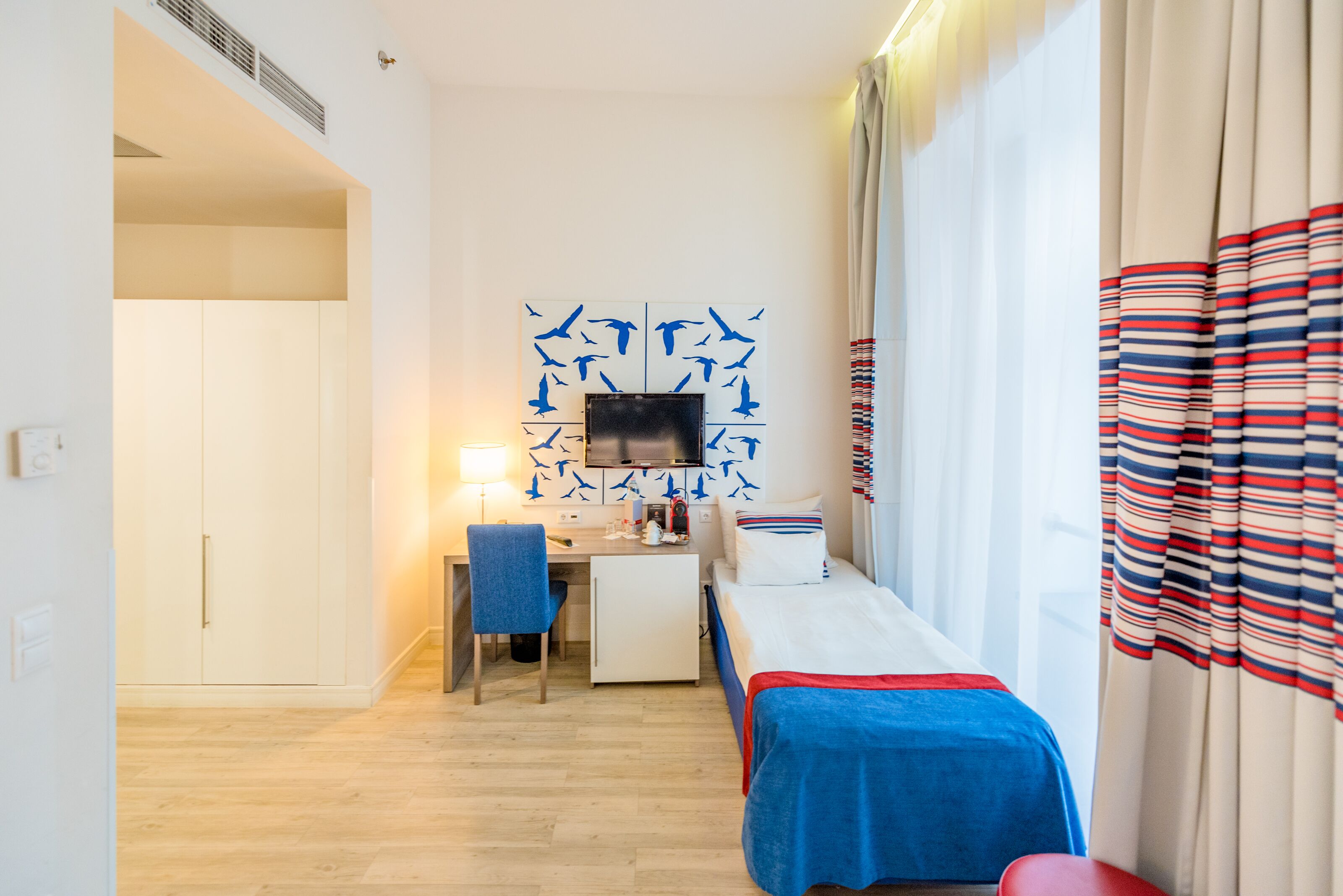 Een hotelkamer met een bed, een bureau, een stoel, een televisie en een raam met gordijnen.