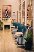 Un hall d'hôtel avec une cheminée, des fauteuils à rayures et une grande affiche représentant un phare.