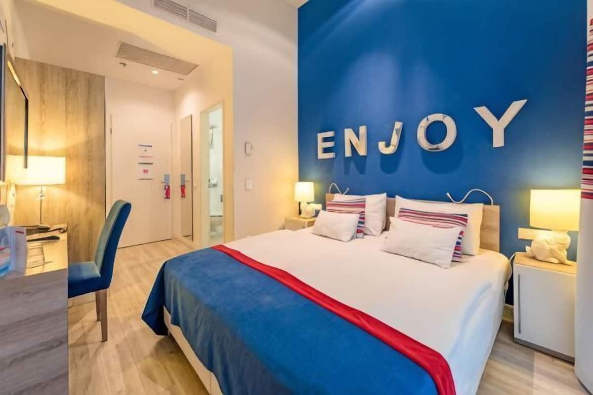 A hotel room with a bed, bedside tables, a desk, and a chair.