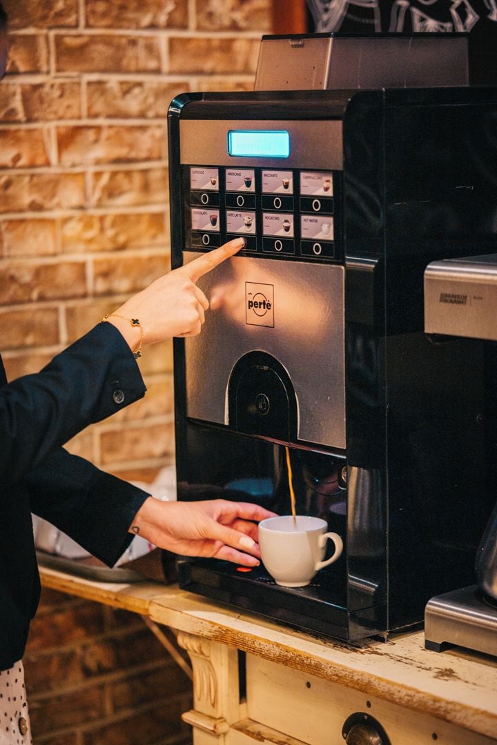 A person using a coffee machine with a digital display and multiple buttons, dispensing coffee into a cup.