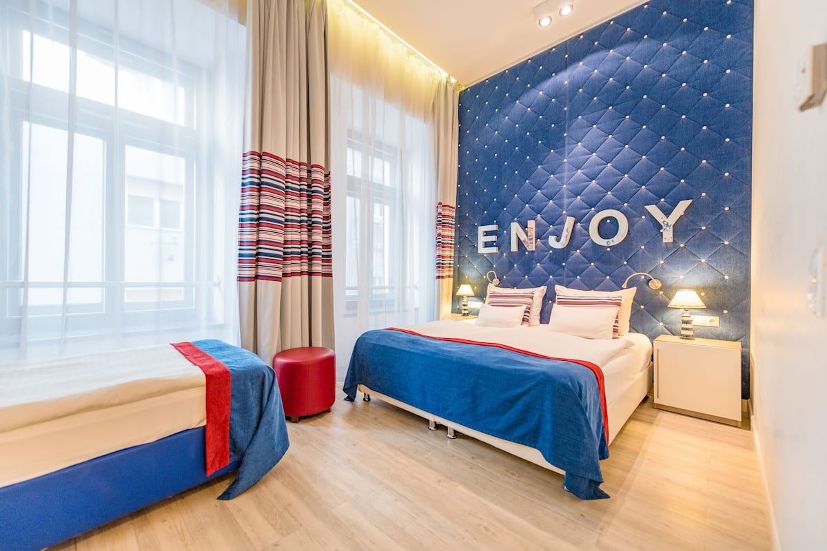 A hotel room with two beds, a red ottoman, and a wall with 'ENJOY' written on it.