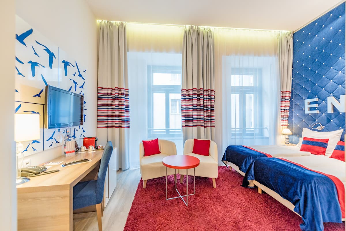 A hotel room with a desk, two chairs, a bed, and a TV.