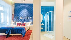 Camera d'albergo moderna con un letto, un tappeto rosso e una parete blu con la scritta 'ENJOY'.