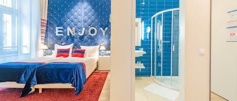 A modern hotel room with a bed, a red rug, and a blue accent wall with 'ENJOY' written on it.