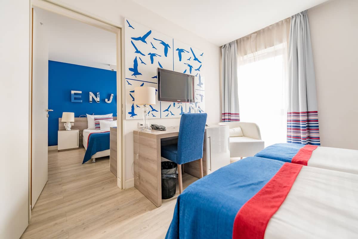 A hotel room with a bed, a desk, a chair, a TV, and a wall with a blue mural.