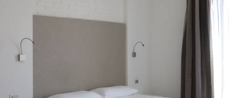 A modern hotel room with a single bed, a bedside table, a lamp, and a window with curtains.