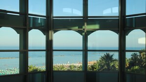 A view through a glass structure with multiple windows, overlooking a beach with umbrellas and palm trees. - Smeraldo Suites & Spa (San Benedetto del Tronto)