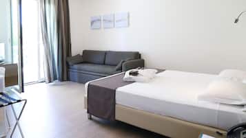 Una camera d'albergo con un letto, un divano, una scrivania con una sedia e un bagno visibile attraverso una porta di vetro.