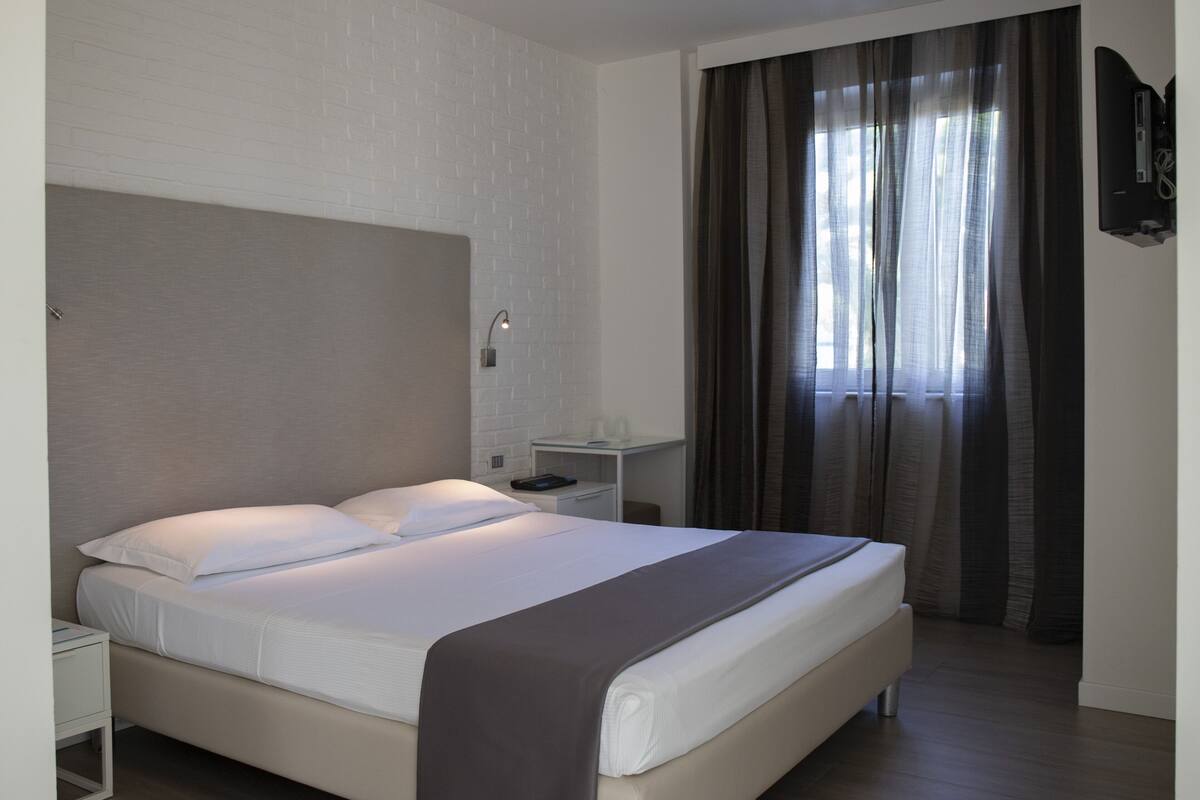 A modern hotel room with a large bed, a bedside table, a nightstand, and a wall-mounted TV.