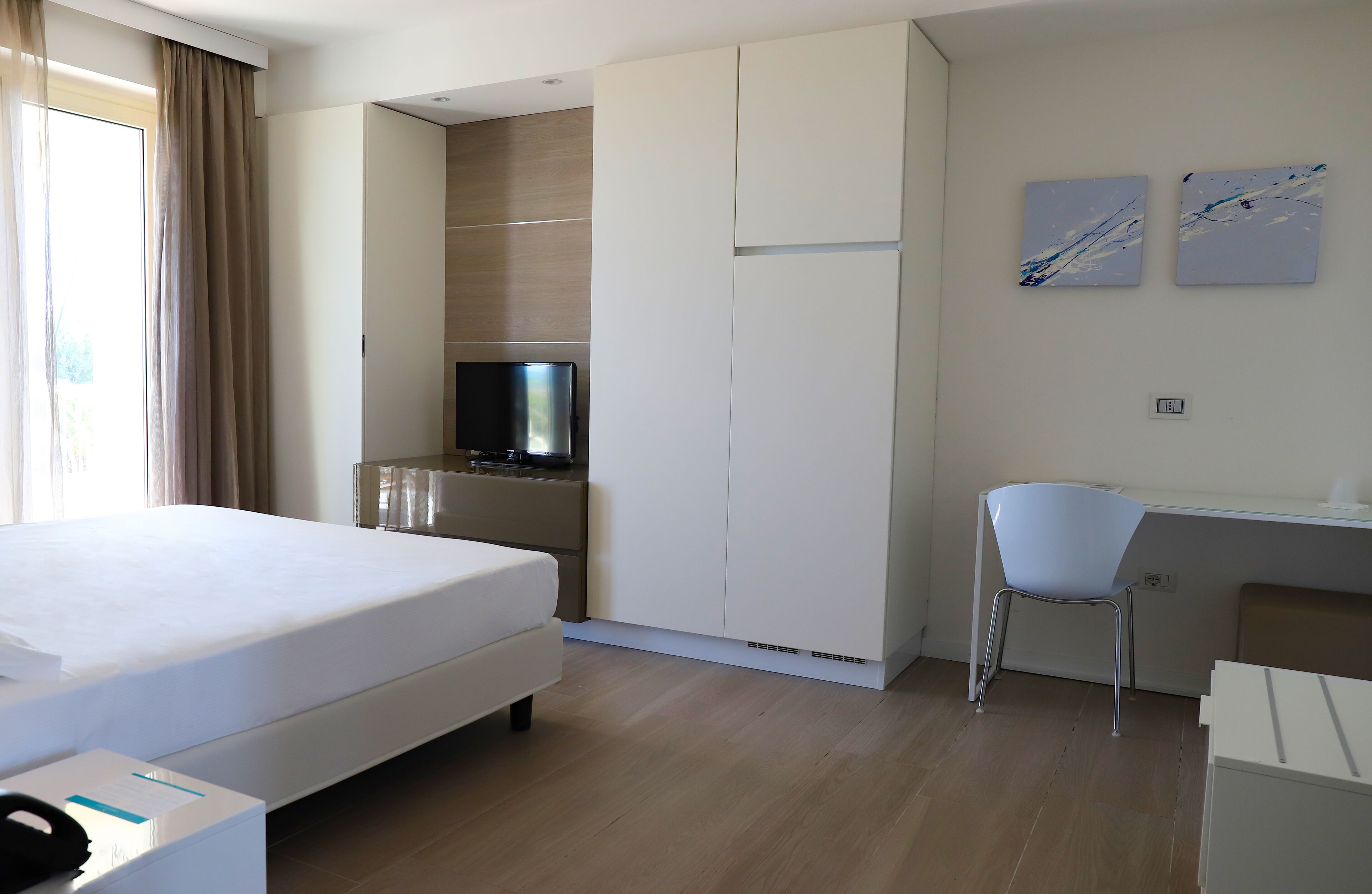 A hotel room with a bed, a desk, a chair, a television, and artwork on the wall.
