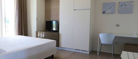 A hotel room with a bed, a desk, a chair, a television, and artwork on the wall.