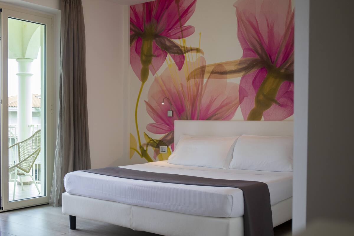 A modern bedroom with a large bed, a view of the outside balcony, and a floral wall mural.