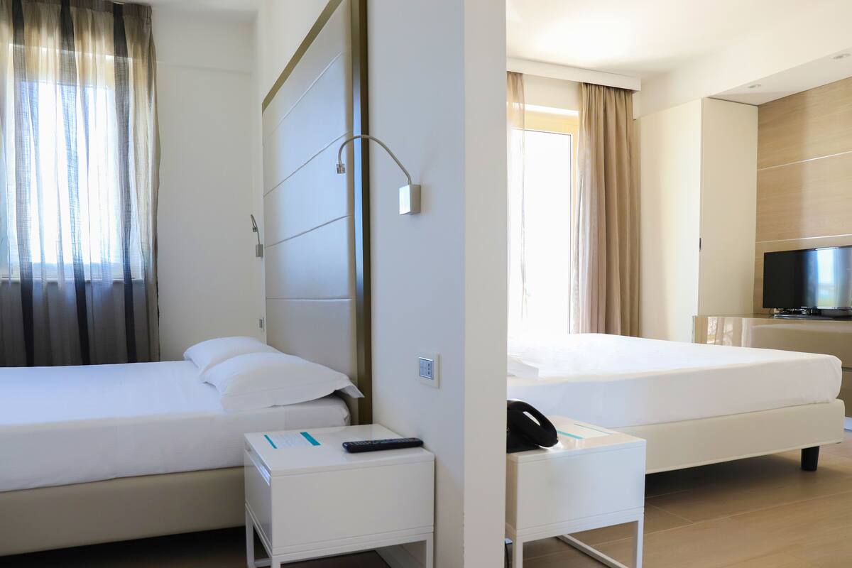 A hotel room with two beds, a TV, a bedside table with a phone, and a window with curtains.