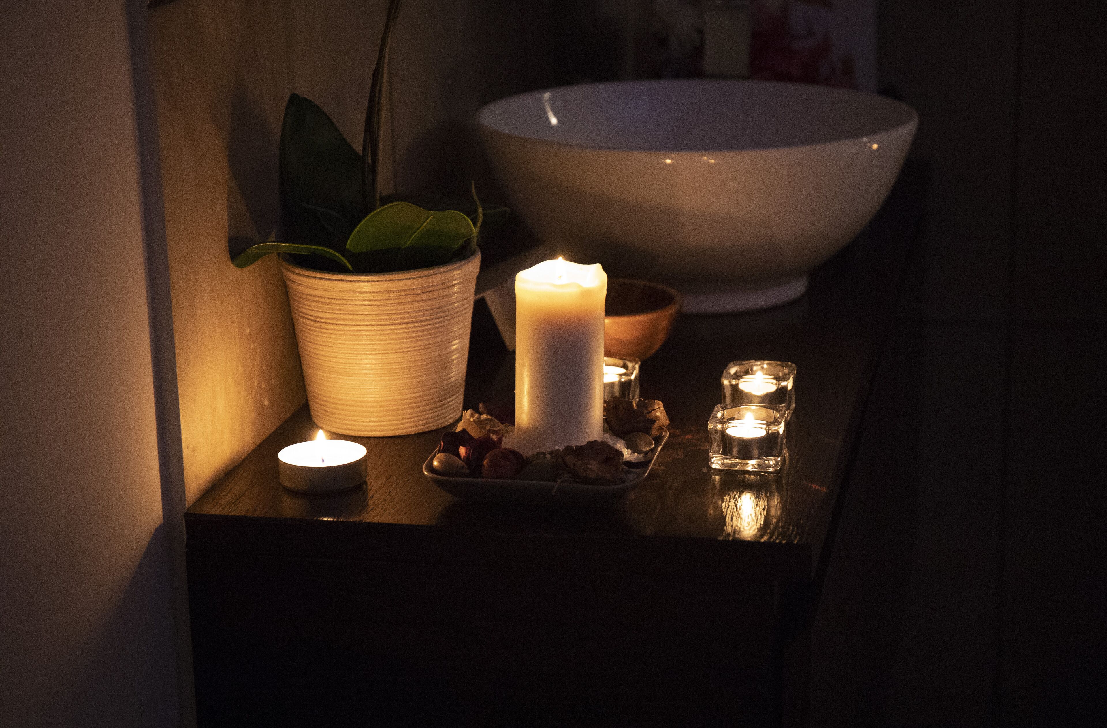 A dimly lit room with a white bowl, a lit candle, and a potted plant on a wooden surface.