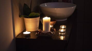 A dimly lit room with a white bowl, a lit candle, and a potted plant on a wooden surface.