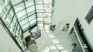 A modern atrium with glass walls, a central staircase, and multiple seating areas. - Smeraldo Suites & Spa (San Benedetto del Tronto)
