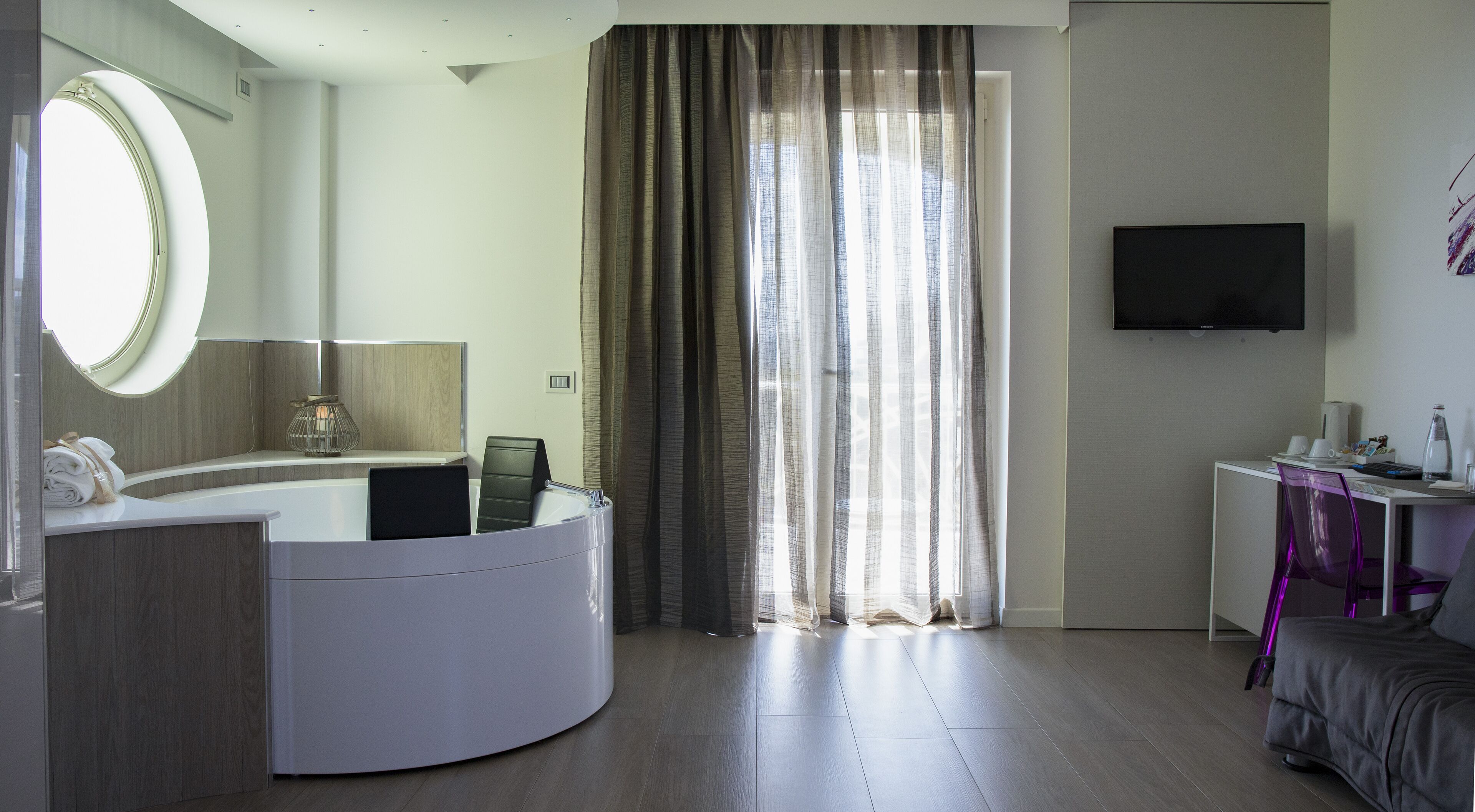 Quarto de hotel moderno com toucador curvo, um espelho grande, televisão de ecrã plano, secretária com cadeira e cama.