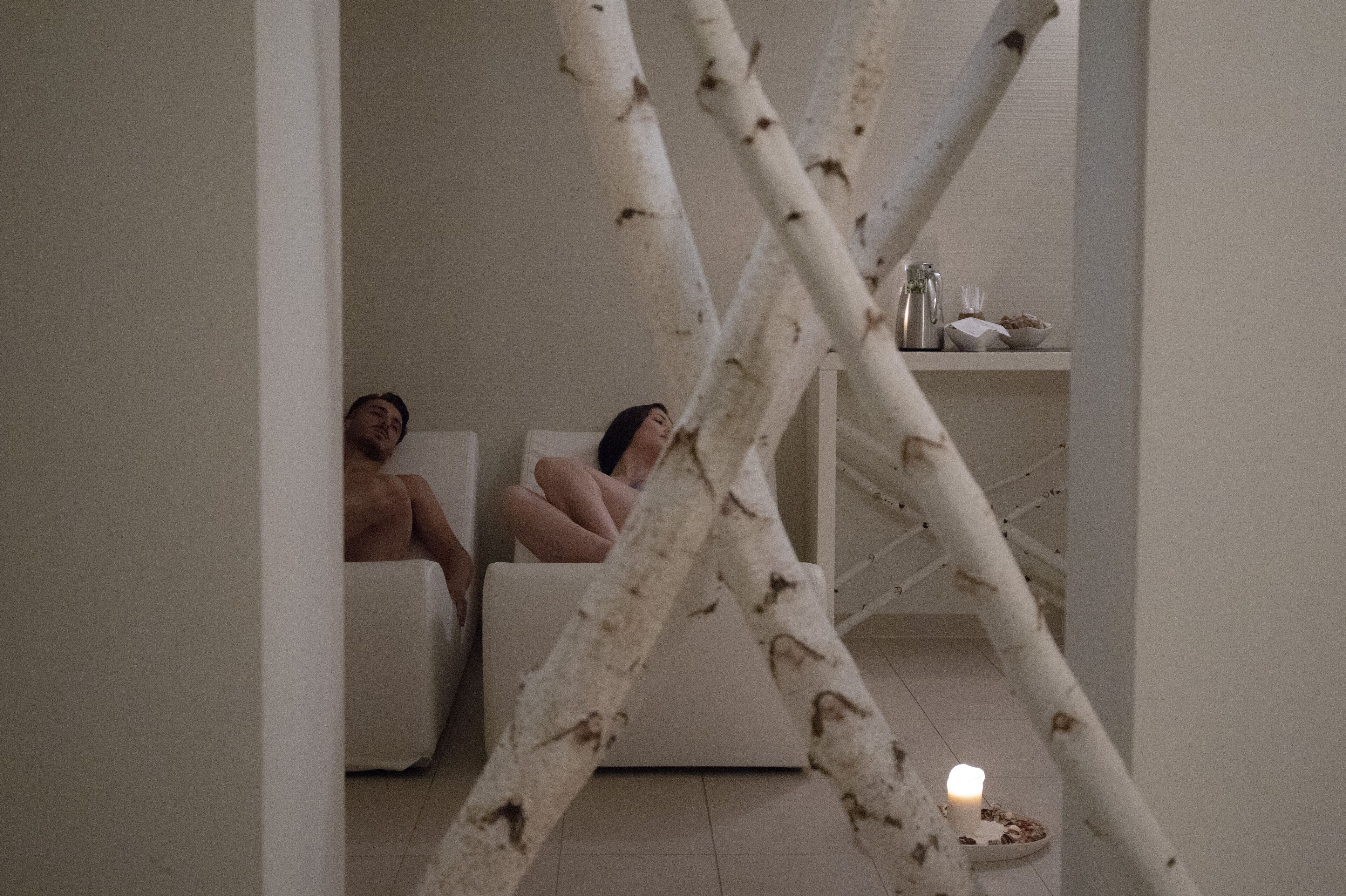 Une pièce avec un canapé blanc, une petite table sur laquelle est posée une bougie, et des branches de bouleau au premier plan.