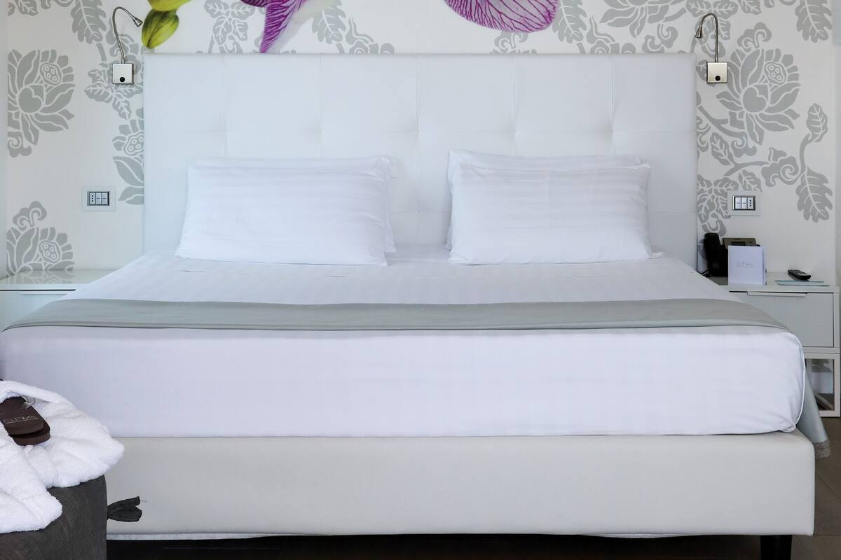 A bedroom with a large bed, white bedding, and a wall-mounted orchid decoration.