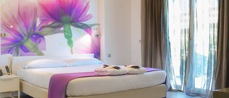 Una habitación de hotel con cama, mesita de noche, lámpara de pared y ventana con cortinas.