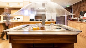 Un espace buffet délimité par une paroi en verre, doté d’un comptoir en bois et proposant une variété de plats.