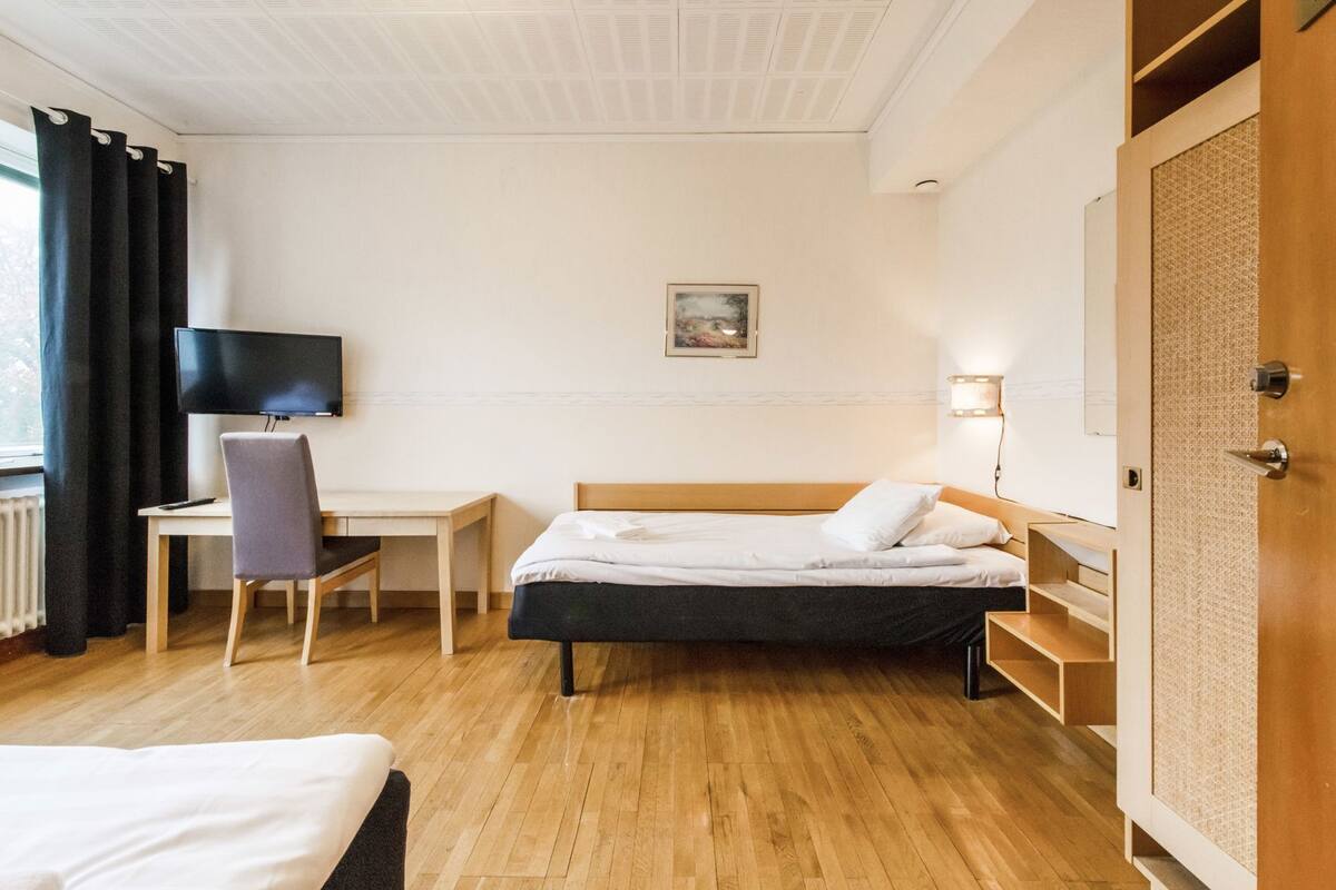 Hotellihuone, jossa on sänky, työpöytä, tuoli, televisio ja ovi, jossa on kuvioitu paneeli.