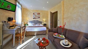 Habitación de hotel con cama, escritorio, televisor, sofá y una mesita con sombrero y flores.
