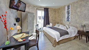 Habitación de hotel con cama, escritorio con silla, televisión montada en la pared y ventana con cortinas.