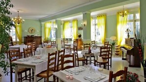 Comedor con mesas dispuestas para el servicio, sillas de madera y un piano al fondo.