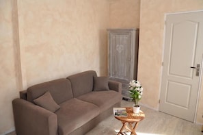 A living room with a brown sofa, a small wooden side table with a potted plant, and a white door. - Hotel Le Lascaux (Montignac)