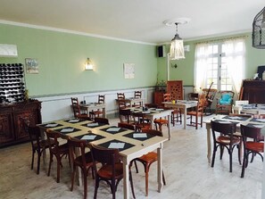 A dining area with multiple tables and chairs, a wooden cabinet, and a chandelier. - Hotel Le Lascaux (Montignac)