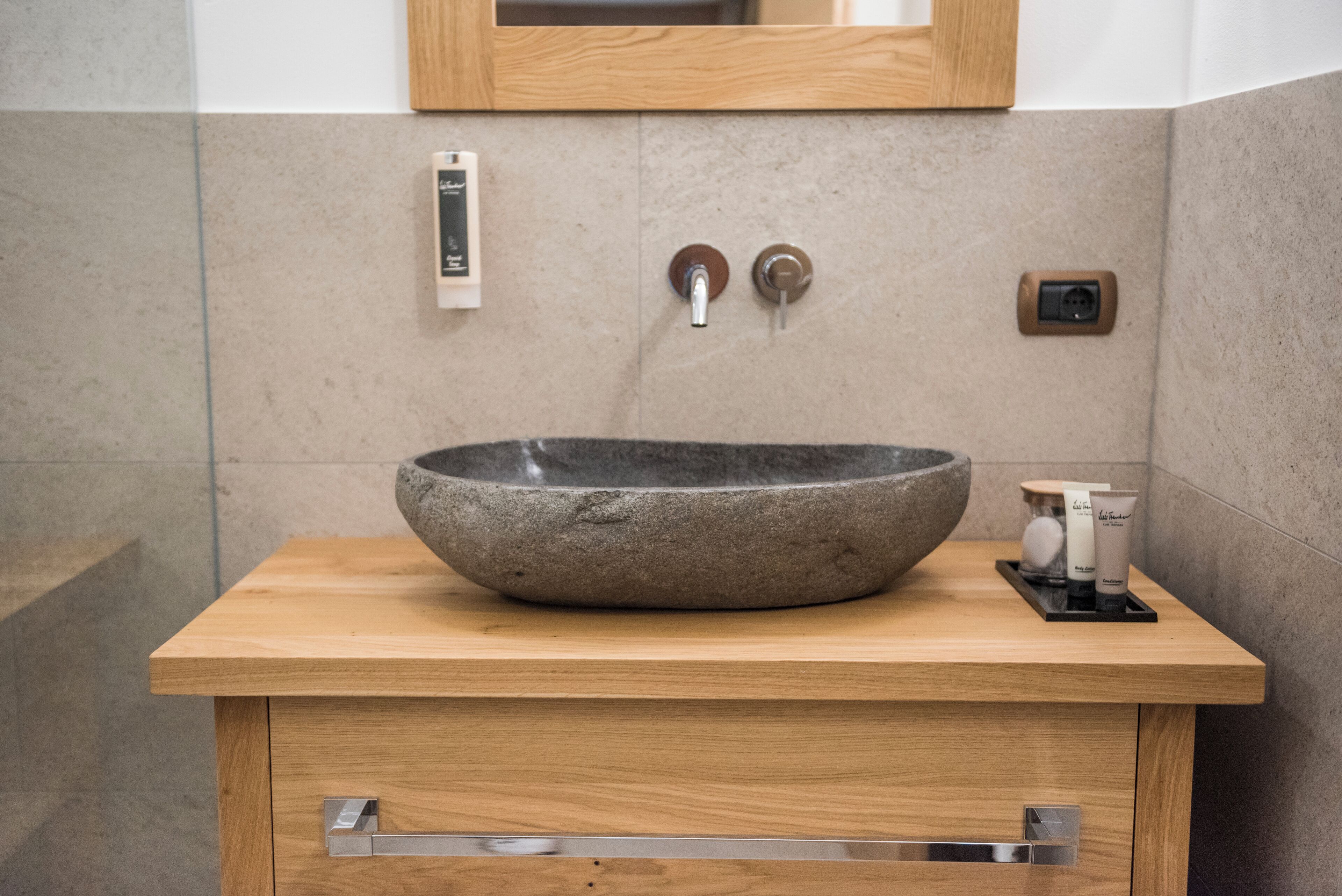 Un baño con lavamanos de piedra, tocador de madera y un espejo sobre el lavamanos.