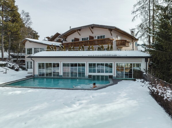 Un edificio moderno con piscina rodeada de nieve, con amplias ventanas y un balcón de madera.