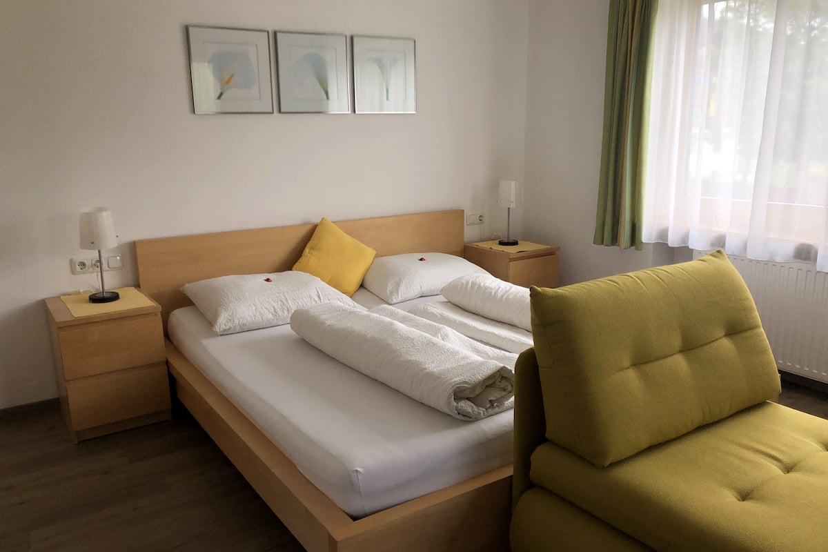 A hotel room with a wooden bed, two bedside tables, a green armchair, and three framed pictures on the wall.
