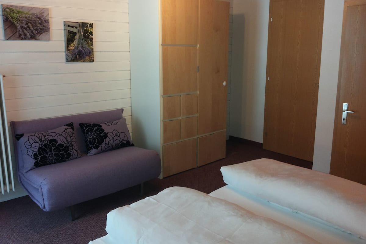 A room with a sofa, a wardrobe, and a bed.
