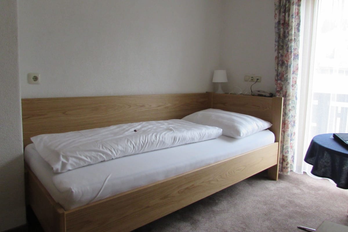 A single bed with a wooden headboard in a hotel room.
