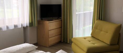 A bedroom with a bed, a TV on a wooden dresser, and a yellow armchair.