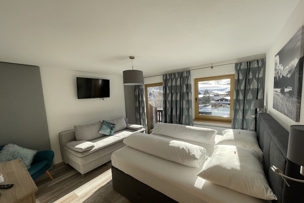 A modern bedroom with a bed, a sofa, a TV, and a window with curtains.