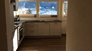 Une cuisine avec des meubles en bois, un fourneau et une vue sur un paysage enneigé, visible à travers de grandes fenêtres.